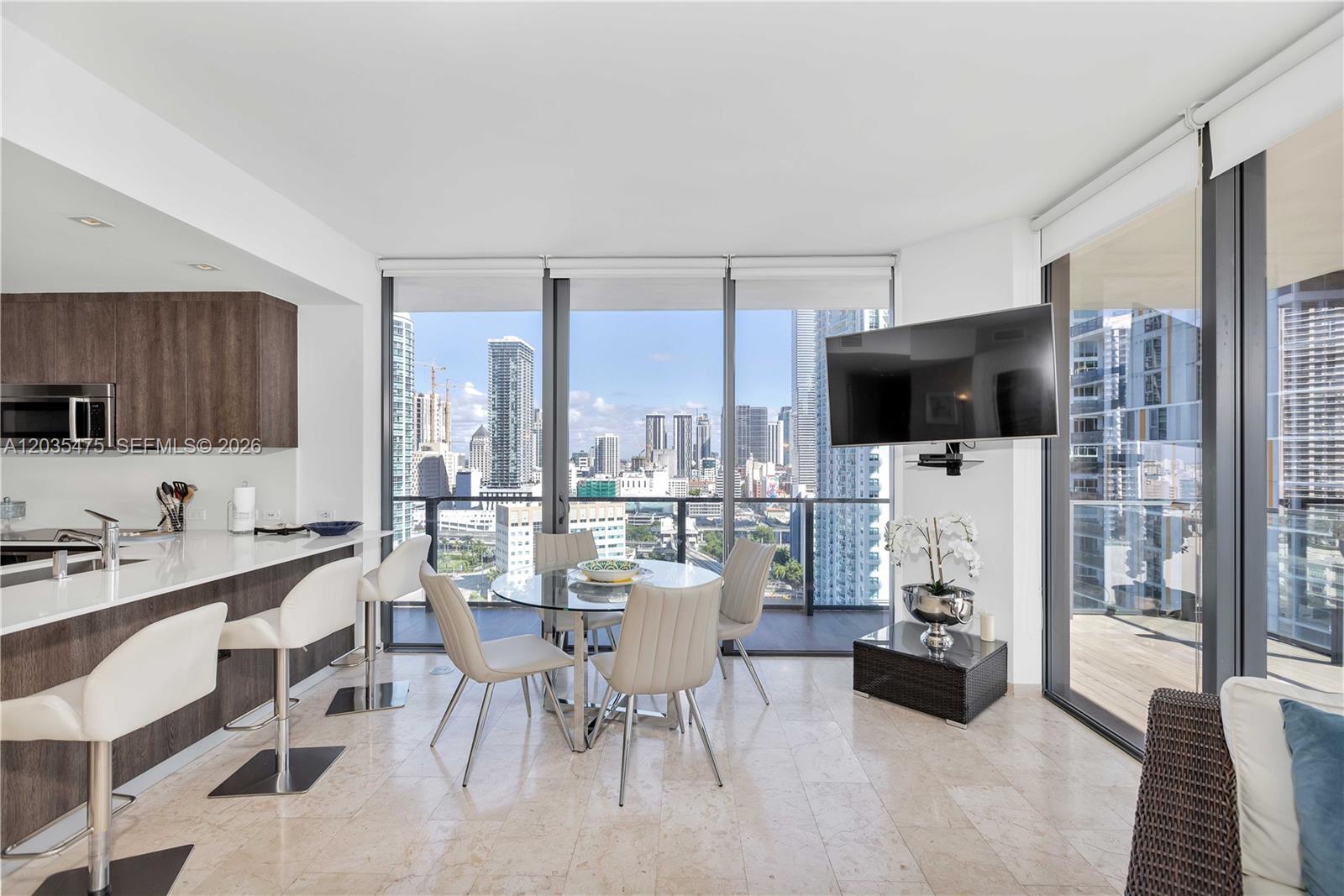 A modern apartment living area features a kitchen island, dining set, and floor-to-ceiling windows — 68 SE 6th St # 1611, Miami FL 33131, MIAMI, FL