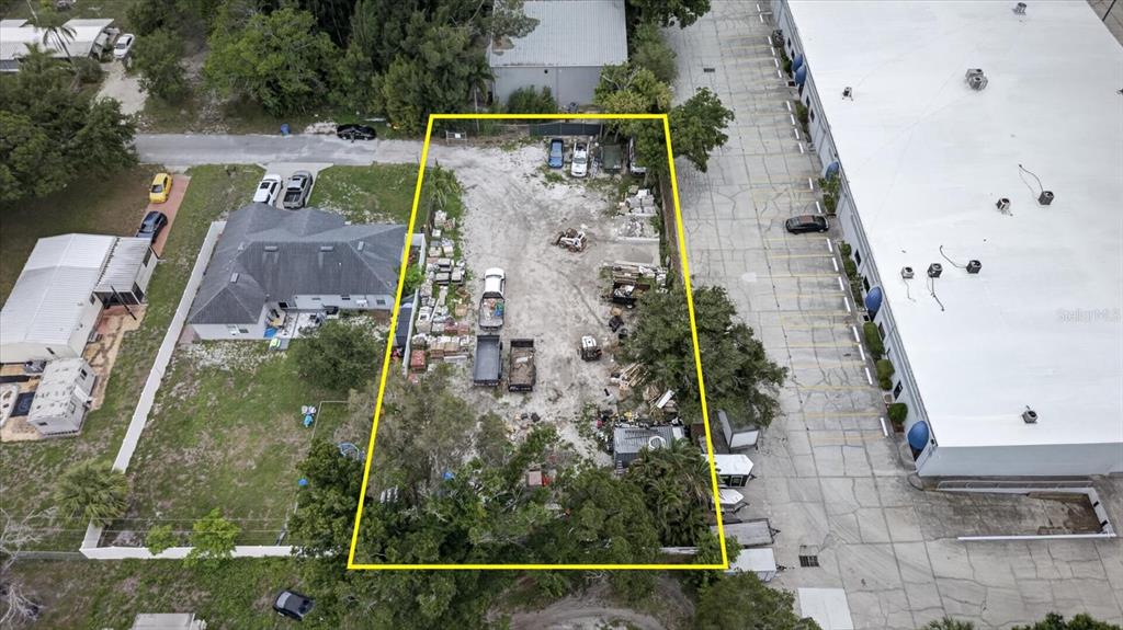 An aerial view shows a rectangular vacant lot filled with debris between a house and warehouse — 6353 143RD AVENUE, CLEARWATER, FL