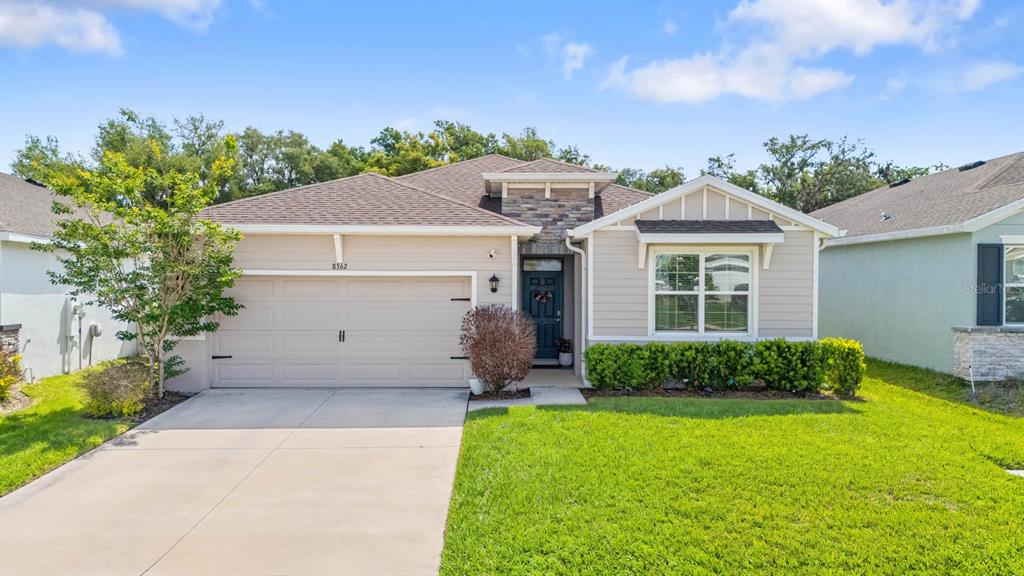A single-story house features a tan exterior, a two-car garage, and a stone-accented entryway — 8362 WHEAT STONE DRIVE, ZEPHYRHILLS, FL