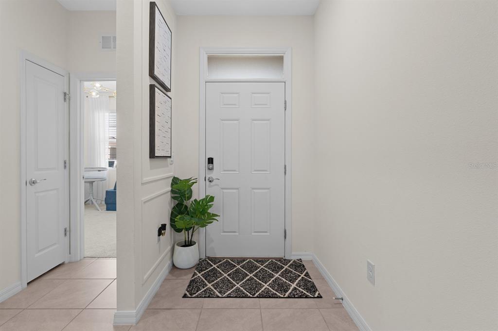 An entryway features a white front door, tiled flooring, a small plant, and wall art — 8362 WHEAT STONE DRIVE, ZEPHYRHILLS, FL