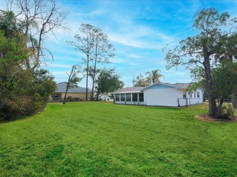 A grassy backyard view of a white house with a screened-in porch and tall trees — 1 Westcliffe Lane, Palm Coast FL 32164, PALM COAST, FL