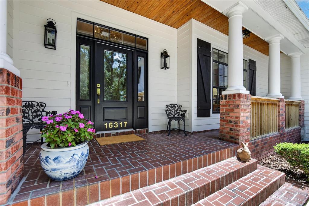A covered brick porch features a black front door, white siding, and decorative columns — 16317 EMERALD COVE, LUTZ, FL