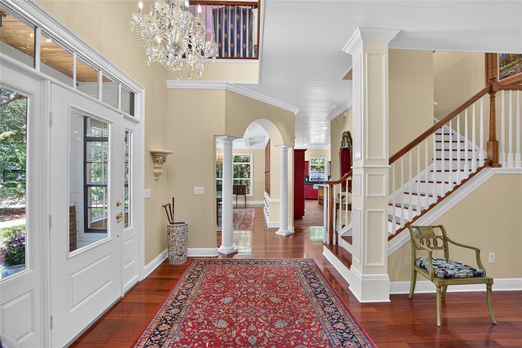 A foyer with hardwood floors, a red area rug, a chandelier, and a wooden staircase — 16317 EMERALD COVE, LUTZ, FL