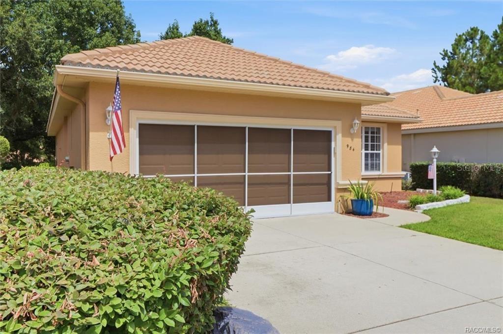 The exterior of a tan house features a garage with a screen door and landscaping — 984 W SILVER MEADOW LOOP, HERNANDO, FL
