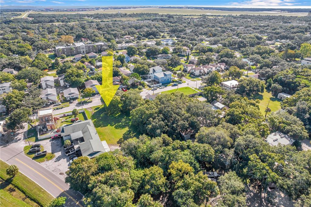An aerial view shows a vacant, tree-lined lot marked by a yellow arrow near buildings — 7111 S KISSIMMEE STREET, TAMPA, FL