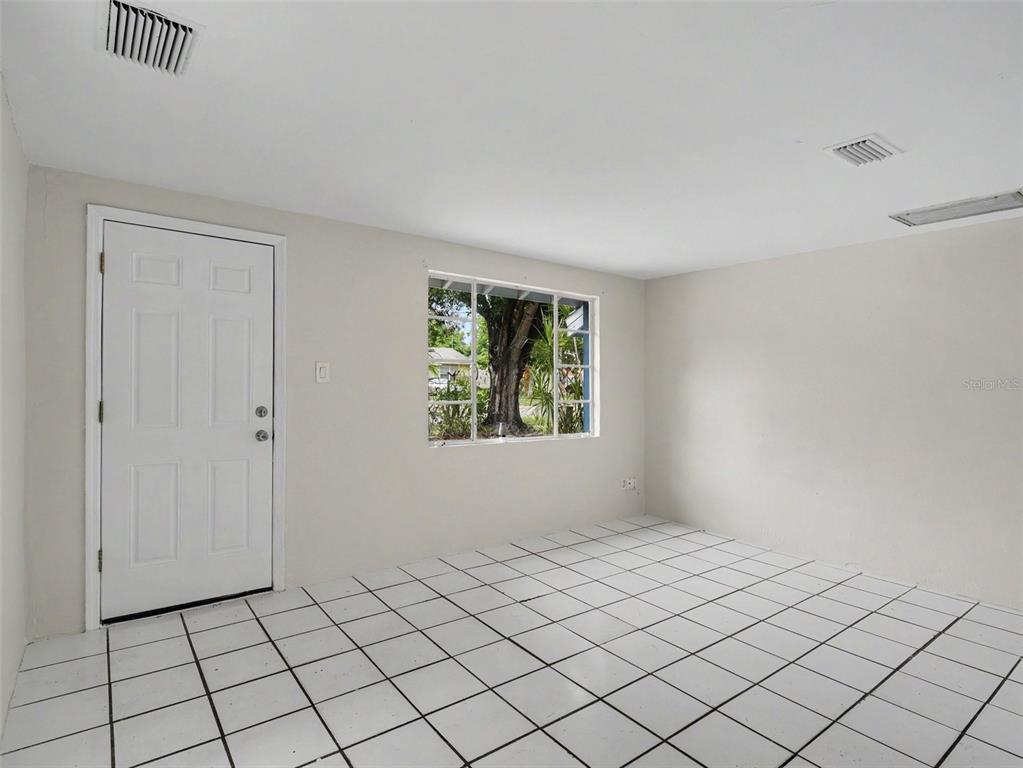 An empty room features white walls, white tiled flooring, a single window, and a white door — 124 26TH AVENUE E UNIT A, BRADENTON, FL
