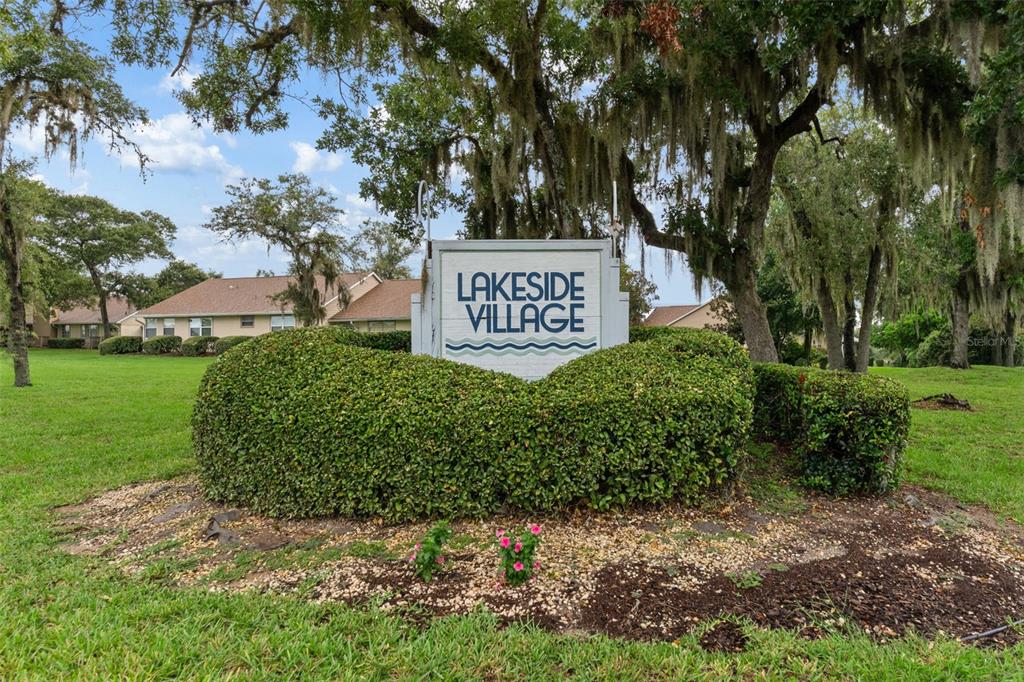 A sign for Lakeside Village stands in front of a green hedge and trees — 3644 N LAURELWOOD LOOP, BEVERLY HILLS, FL