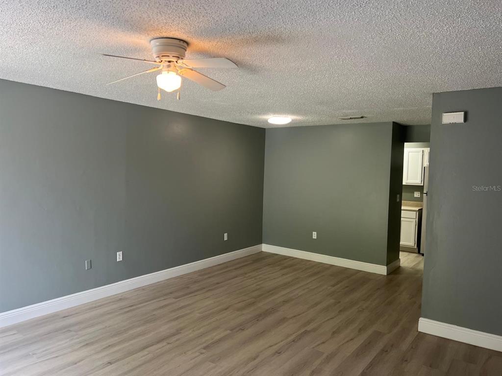 A living room with grey walls, light wood-look flooring, a ceiling fan, and sliding glass doors — 4123 SPITFIRE, KISSIMMEE, FL