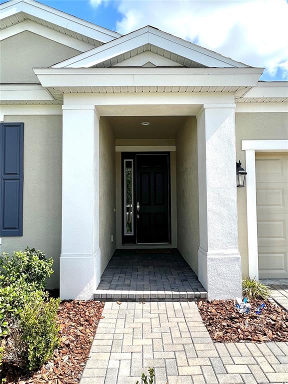 The exterior of a house features a covered entryway with a dark door and pavers — 4786 BALLANTRAE BOULEVARD, LAND O LAKES, FL