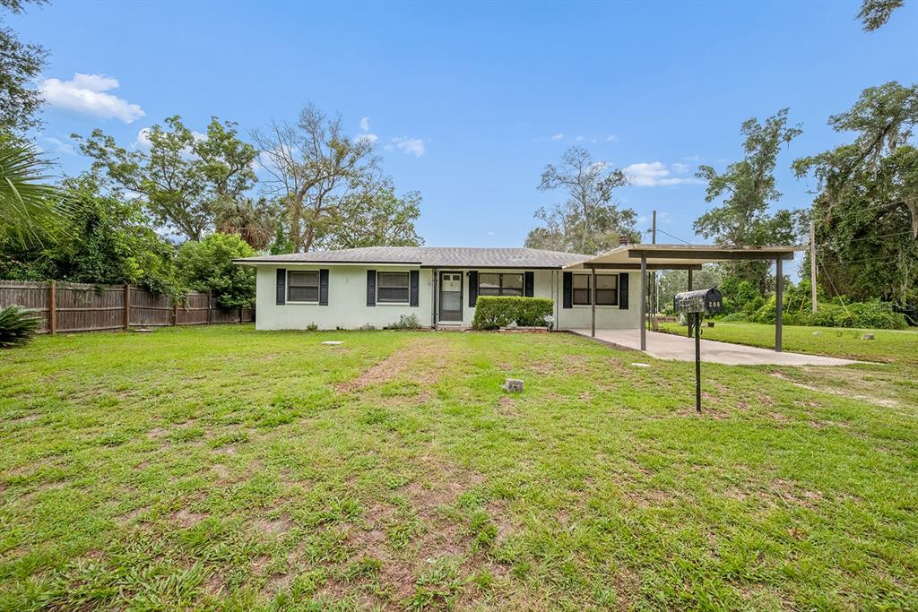A single-story house with a light-colored exterior, a front carport, and a large grassy yard — 206 NE 6TH STREET, TRENTON, FL