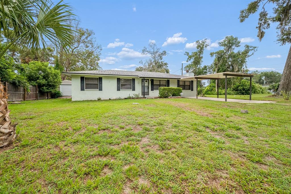 A single-story house with a light-colored exterior, dark window shutters, and an attached metal carport — 206 NE 6TH STREET, TRENTON, FL