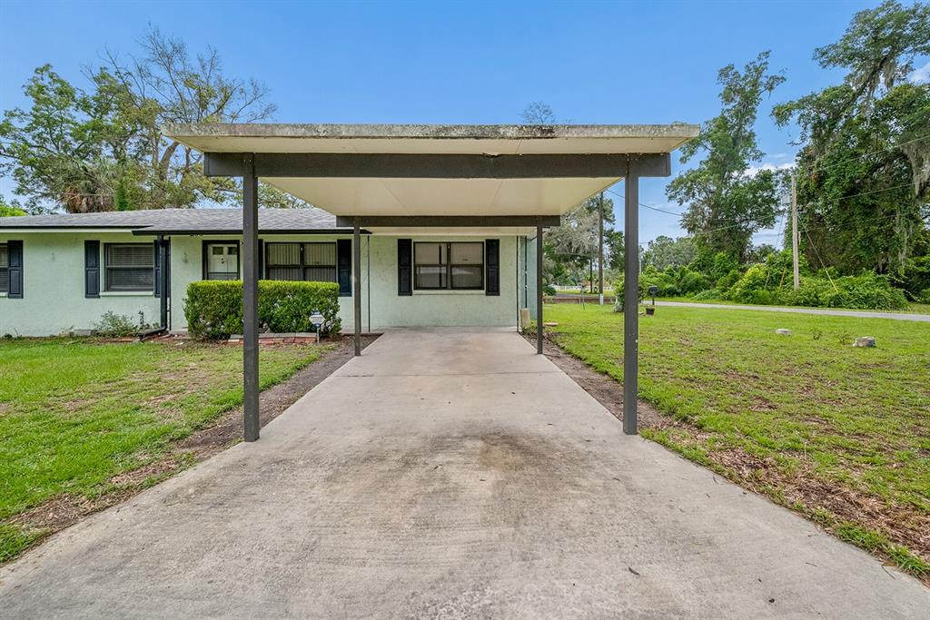 A light green house features a concrete driveway covered by a flat-roofed metal carport — 206 NE 6TH STREET, TRENTON, FL
