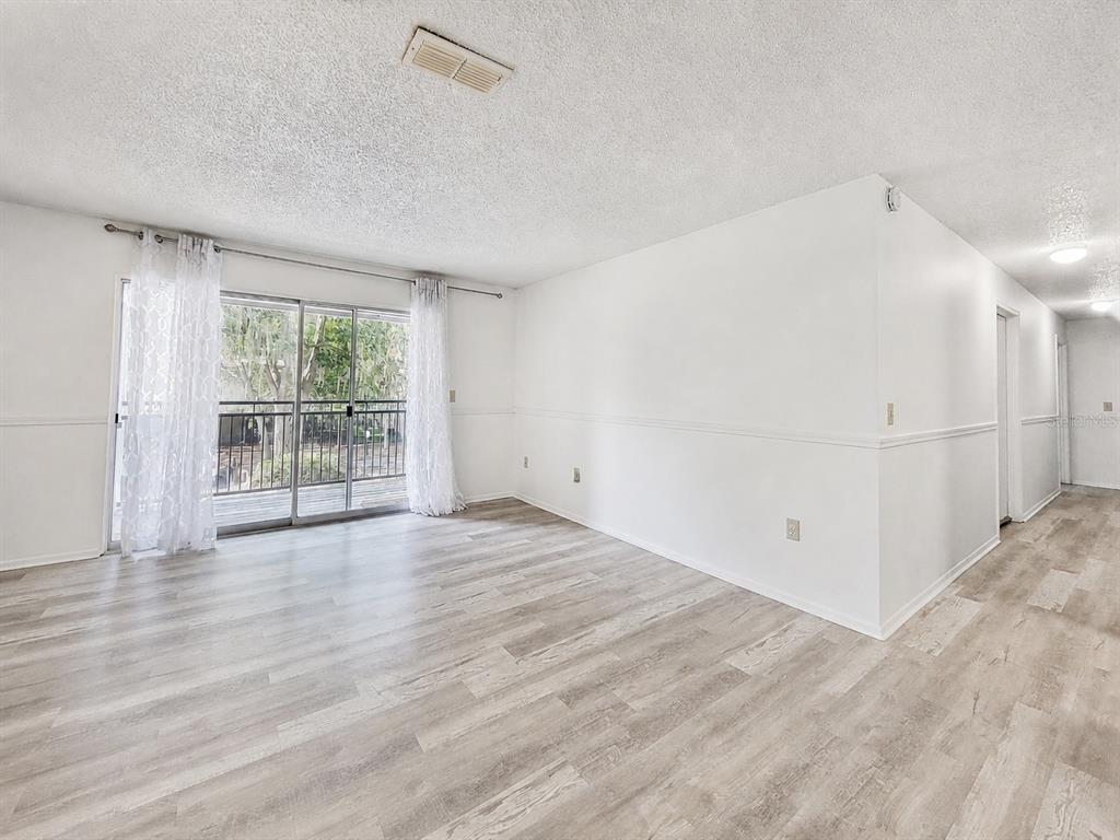 An empty room with light wood-look flooring, white walls, and a sliding glass door — 3705 SW 27TH STREET UNIT 921, GAINESVILLE, FL