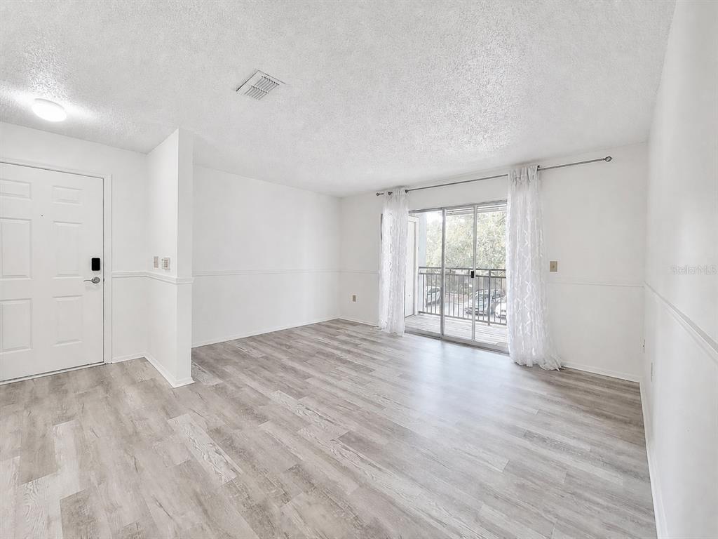 An empty living room features white walls, wood-look flooring, and a sliding glass balcony door — 3705 SW 27TH STREET UNIT 921, GAINESVILLE, FL