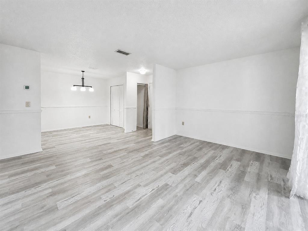 An empty room with light wood-look flooring, white walls, and a dining area light fixture — 3705 SW 27TH STREET UNIT 921, GAINESVILLE, FL