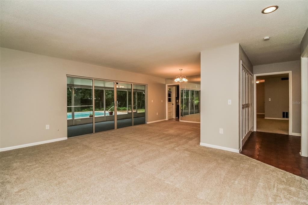 A carpeted living room features a sliding glass door looking out onto a swimming pool — 745 LITTLE WEKIVA CIRCLE, ALTAMONTE SPRINGS, FL