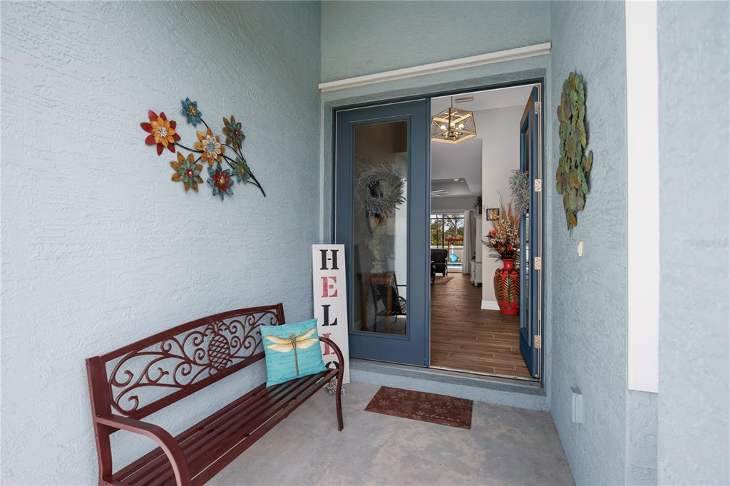 A covered entryway features a metal bench, a dragonfly pillow, and a blue front door — 119 GREEN OAK PARK, ROTONDA WEST, FL