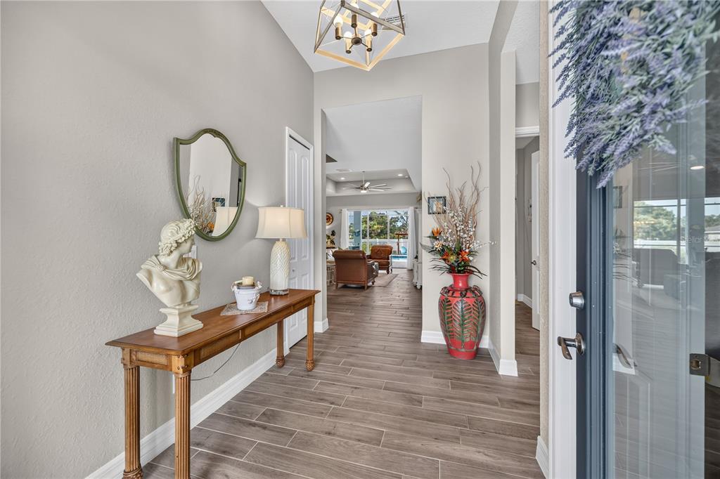 A bright entryway features wood-look tile flooring, a console table with a bust, and a chandelier — 119 GREEN OAK PARK, ROTONDA WEST, FL