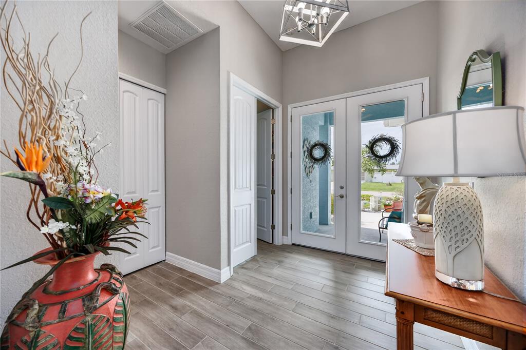 An entryway features light wood-look tile flooring, a decorative vase, and double glass front doors — 119 GREEN OAK PARK, ROTONDA WEST, FL