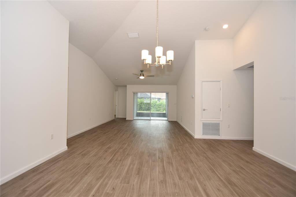 An empty living room features vaulted ceilings, light wood-look flooring, and a sliding glass door — 19 ETHEL LANE, PALM COAST, FL