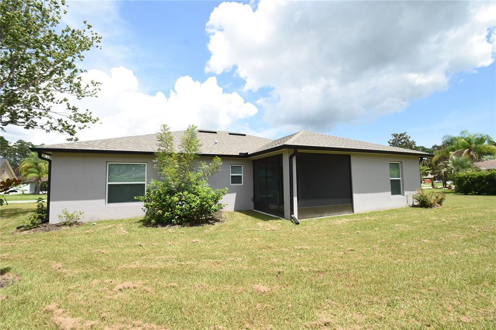The rear exterior of a single-story house features a screened-in porch and a grassy yard — 19 ETHEL LANE, PALM COAST, FL