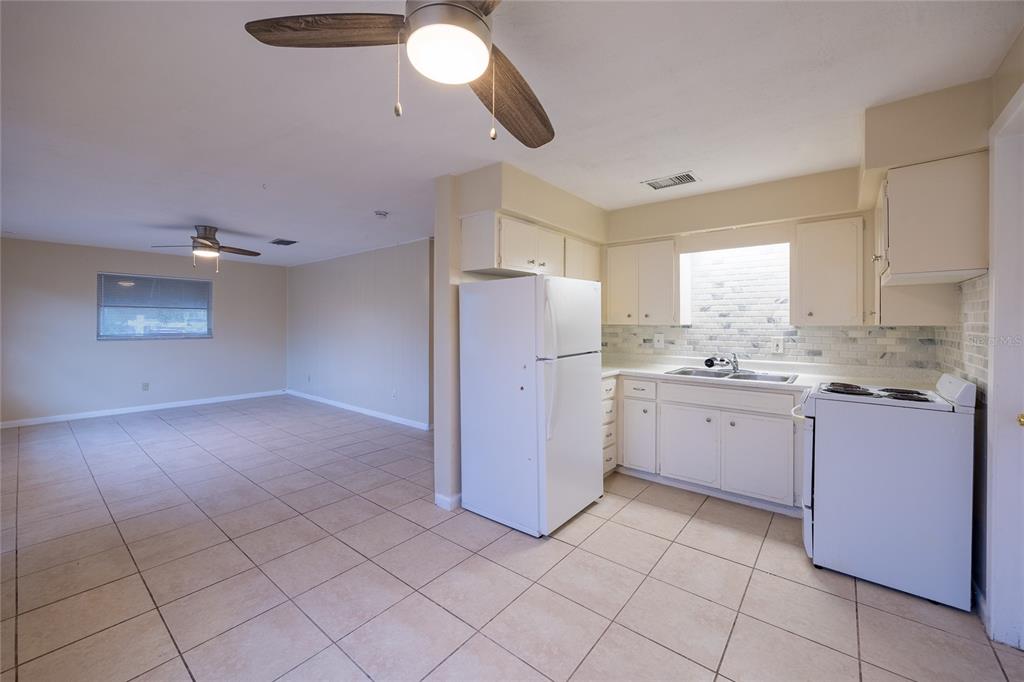 A kitchen with white appliances and cabinets opens into a large, tiled living area — 400 S METEOR AVENUE, CLEARWATER, FL