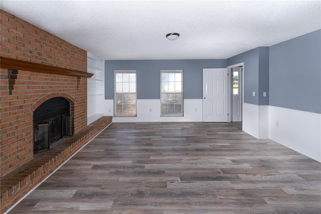 A living room features a brick fireplace, built-in shelving, gray walls with white wainscoting, and wood-look flooring — 5308 COUNTY ROAD 122, WILDWOOD, FL