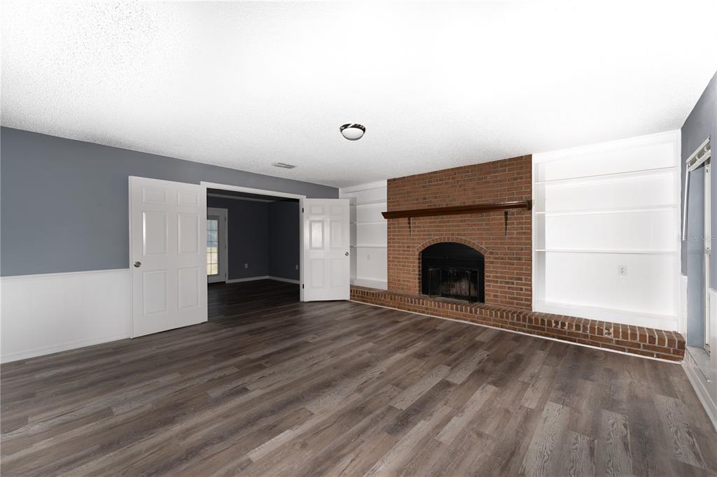 A living room features a brick fireplace, built-in white shelving, and wood-look flooring — 5308 COUNTY ROAD 122, WILDWOOD, FL