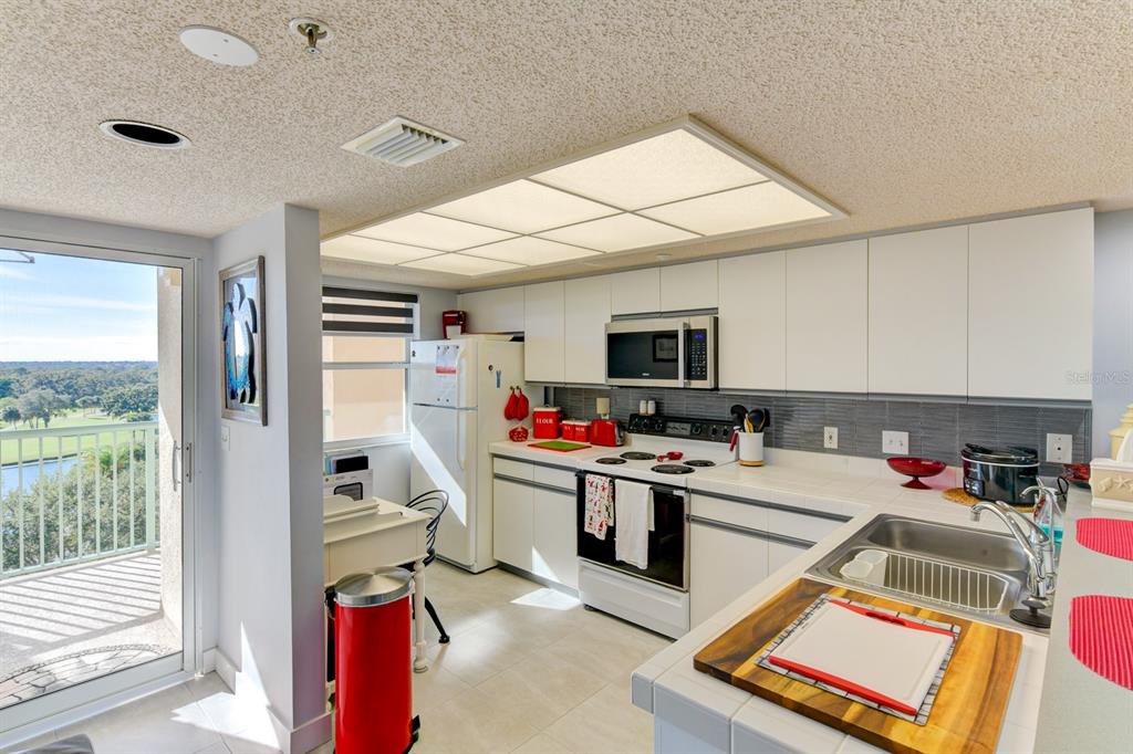 A kitchen with white cabinets, a tile backsplash, and a balcony view of a golf course — 2320 TERRA CEIA BAY BOULEVARD UNIT 811, PALMETTO, FL
