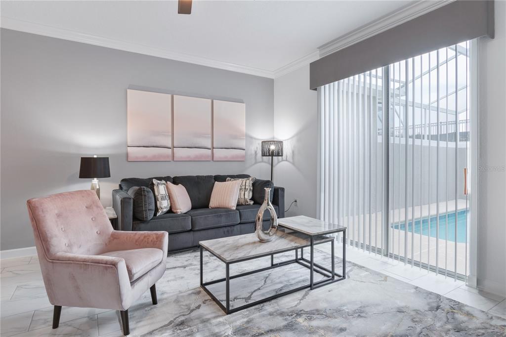 A living room features a dark sofa, a pink armchair, nesting tables, and a pool view — 1060 LEADER STREET, DAVENPORT, FL