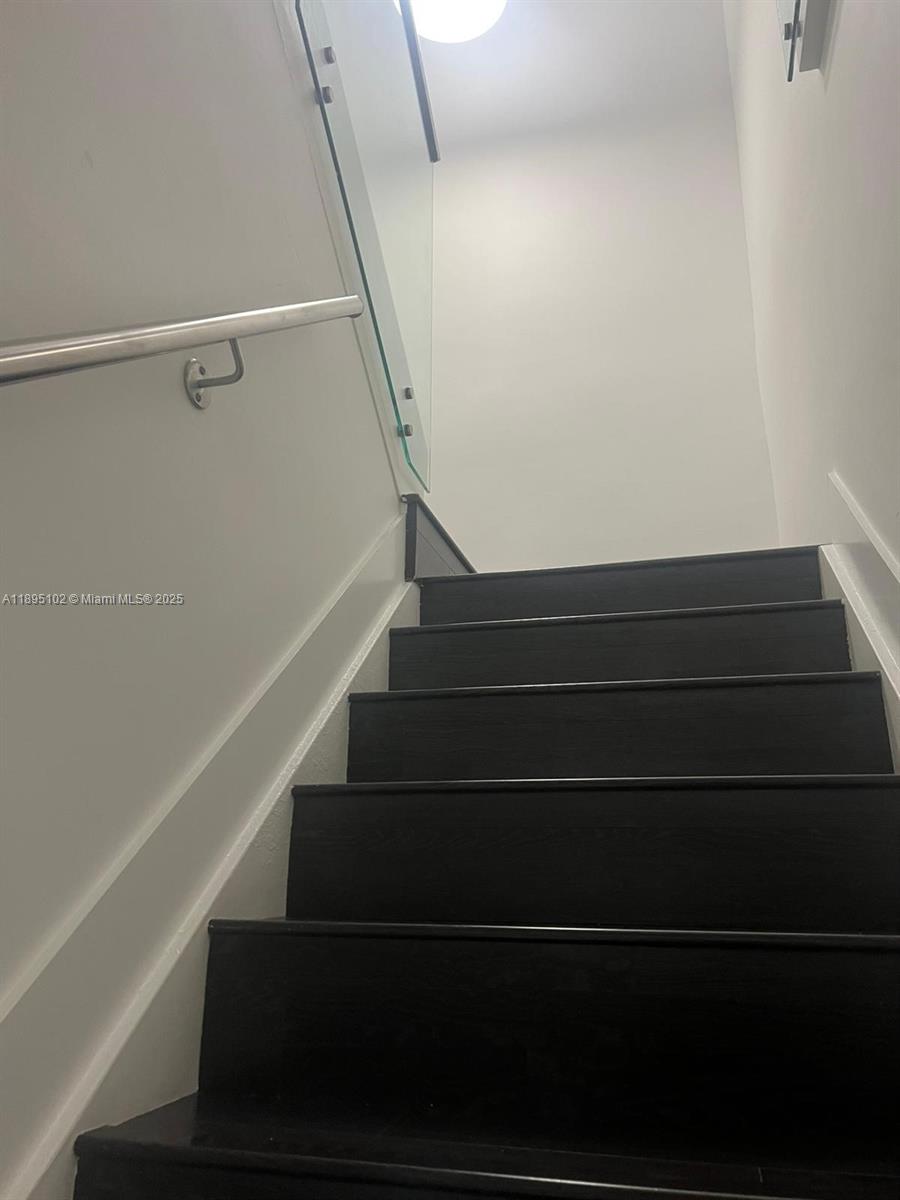 A staircase with dark wood treads leads upward alongside a glass railing and metal handrail — 11281 NW 84th St, Doral FL 33178, DORAL, FL
