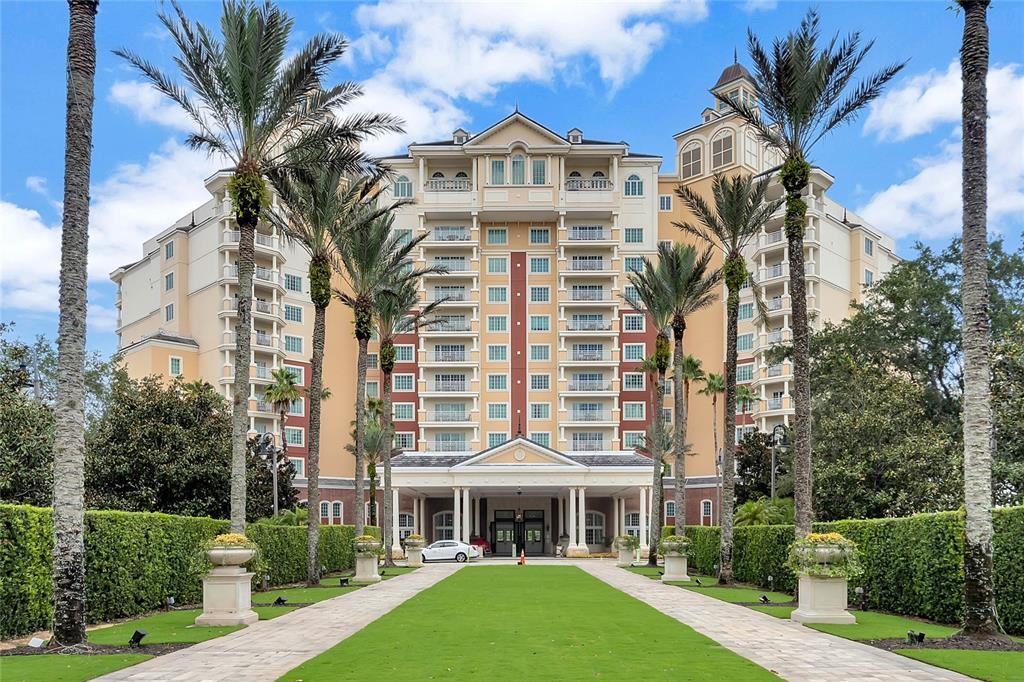 A multi-story hotel building features a central entrance with palm trees and a grassy lawn — 7593 GATHERING DRIVE UNIT 504, KISSIMMEE, FL