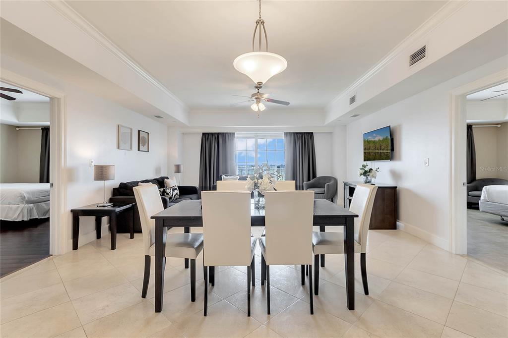A dining area with a dark table and white chairs sits before a living space — 7593 GATHERING DRIVE UNIT 504, KISSIMMEE, FL