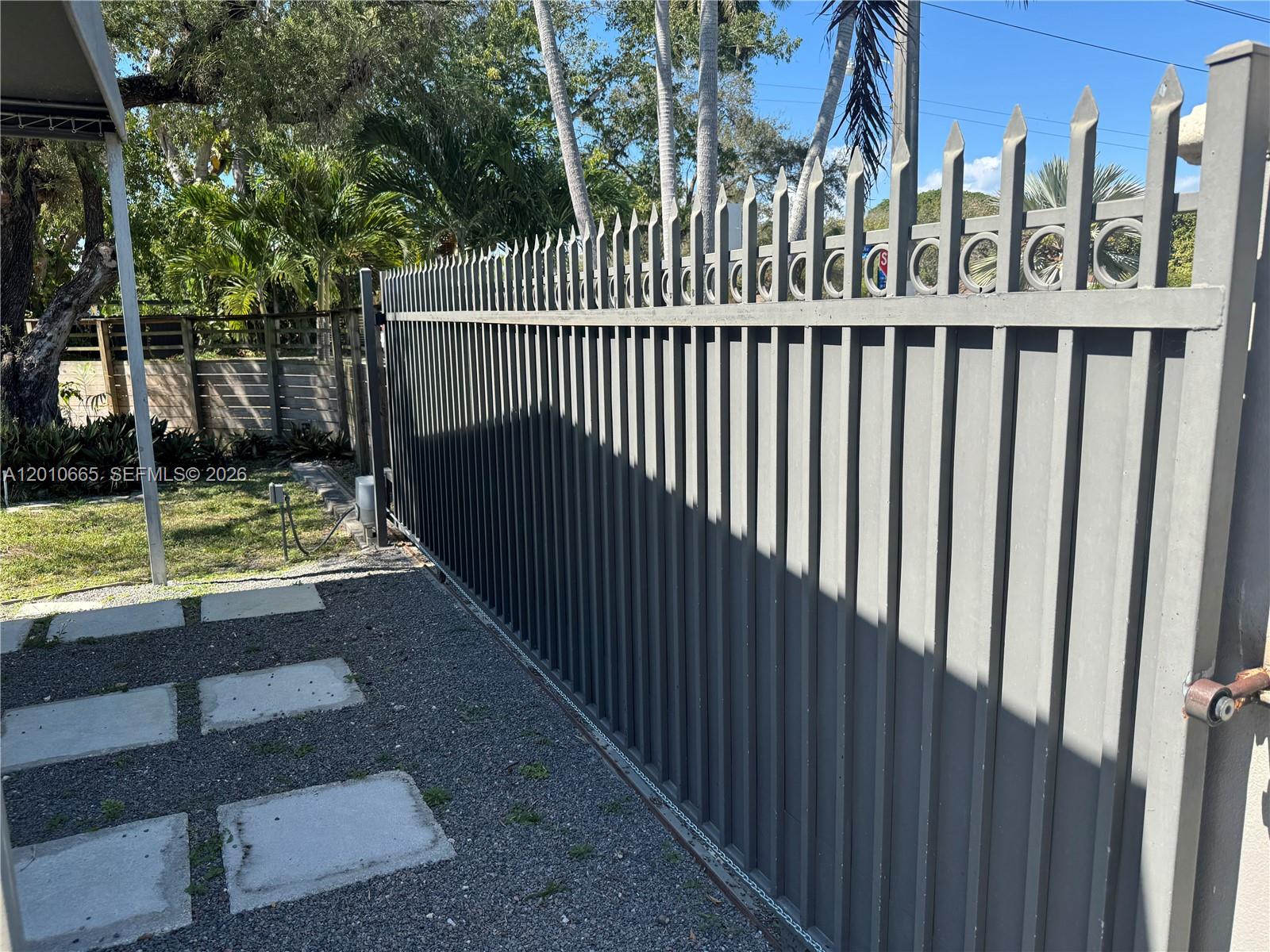 A tall gray metal sliding gate stands in front of a gravel driveway and yard — 3155 SW 132nd Ave, Miami FL 33175, MIAMI, FL