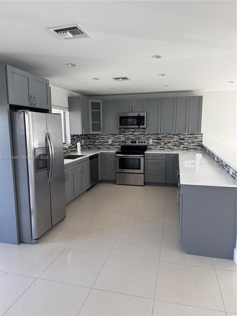 A kitchen features gray cabinets, stainless steel appliances, a tiled backsplash, and white countertops — 3155 SW 132nd Ave, Miami FL 33175, MIAMI, FL
