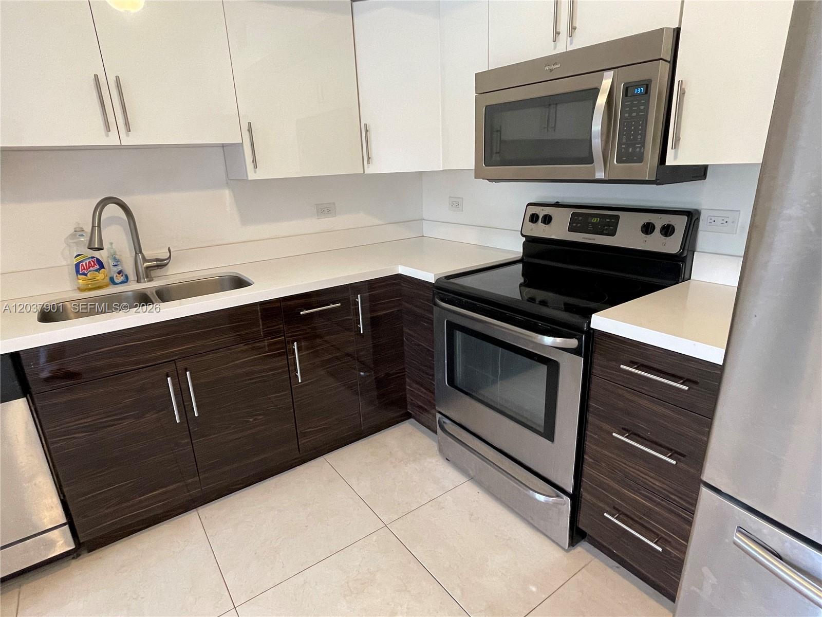 A modern kitchen features white upper cabinets, dark wood lower cabinets, and stainless steel appliances — 3690 N 56th Ave # 904, Hollywood FL 33021, HOLLYWOOD, FL