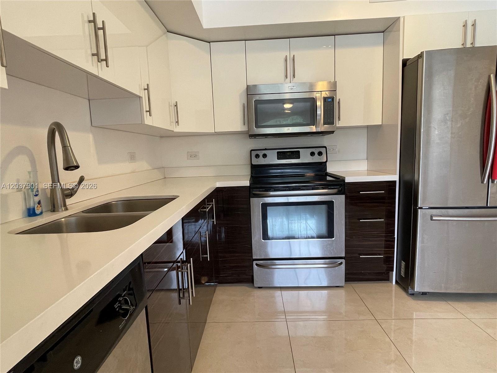 A kitchen features white upper cabinets, dark lower cabinets, stainless steel appliances, and tile flooring — 3690 N 56th Ave # 904, Hollywood FL 33021, HOLLYWOOD, FL