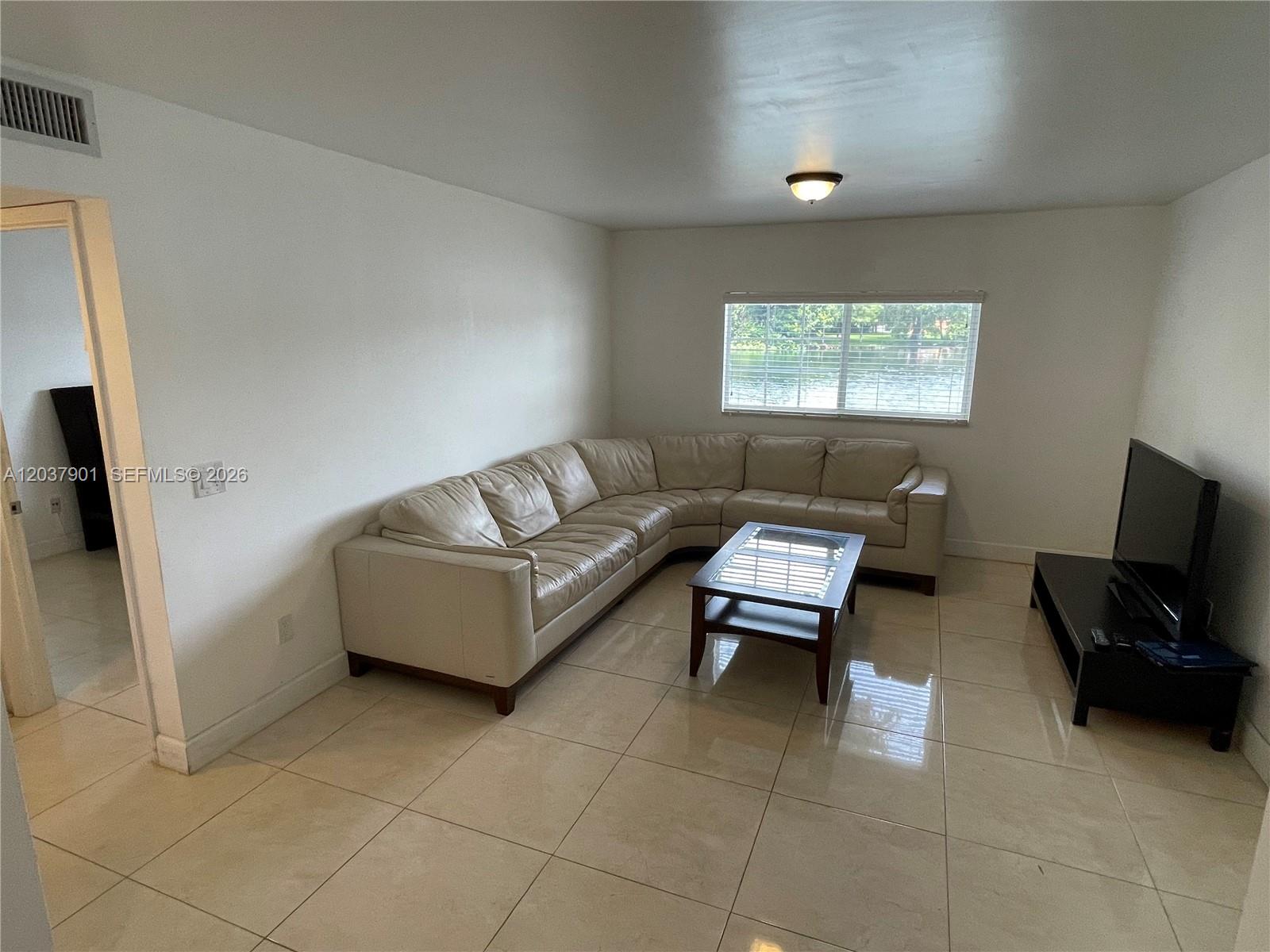 A living room features a large beige sectional sofa, a coffee table, and tile flooring — 3690 N 56th Ave # 904, Hollywood FL 33021, HOLLYWOOD, FL