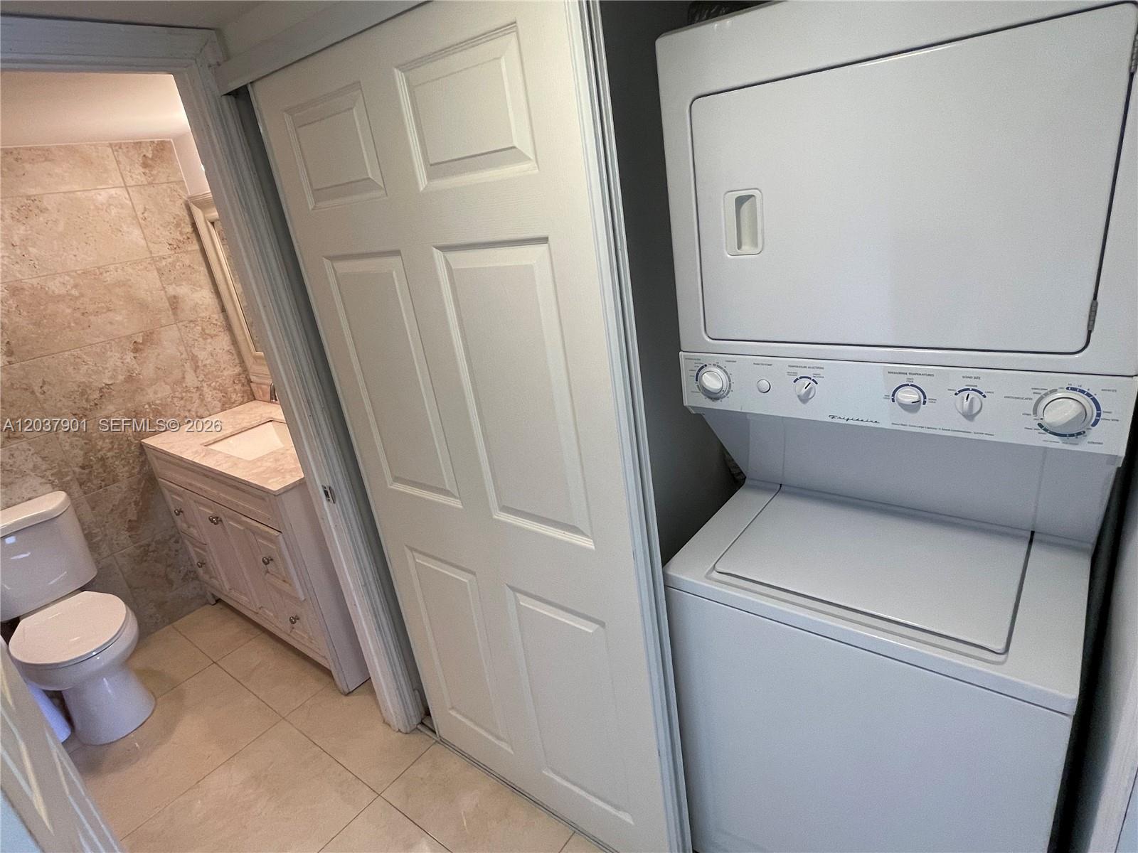 A white stacked laundry unit stands next to a bathroom with a vanity and toilet — 3690 N 56th Ave # 904, Hollywood FL 33021, HOLLYWOOD, FL