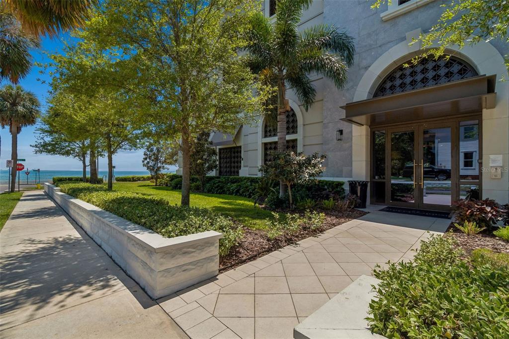 An exterior view of a building entrance with a stone walkway, landscaping, and ocean views — 2103 BAYSHORE BOULEVARD UNIT 1203, TAMPA, FL