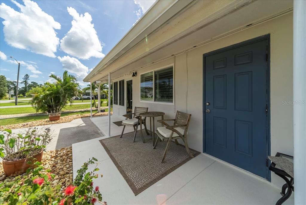 A covered porch features a blue door, a small table with two chairs, and landscaping — 2830 10TH STREET, ENGLEWOOD, FL