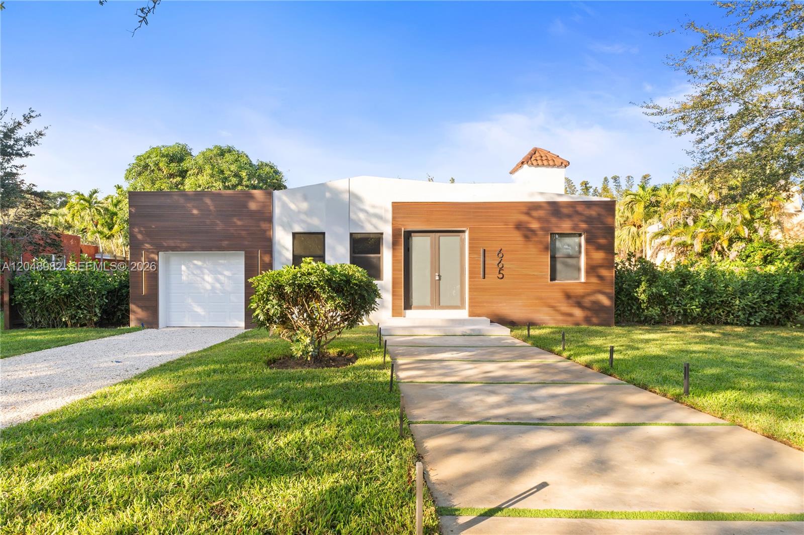 A single-story house features horizontal wood siding, a white stucco center, and a concrete driveway — 665 NE 117th St, Biscayne Park FL 33161, BISCAYNE PARK, FL