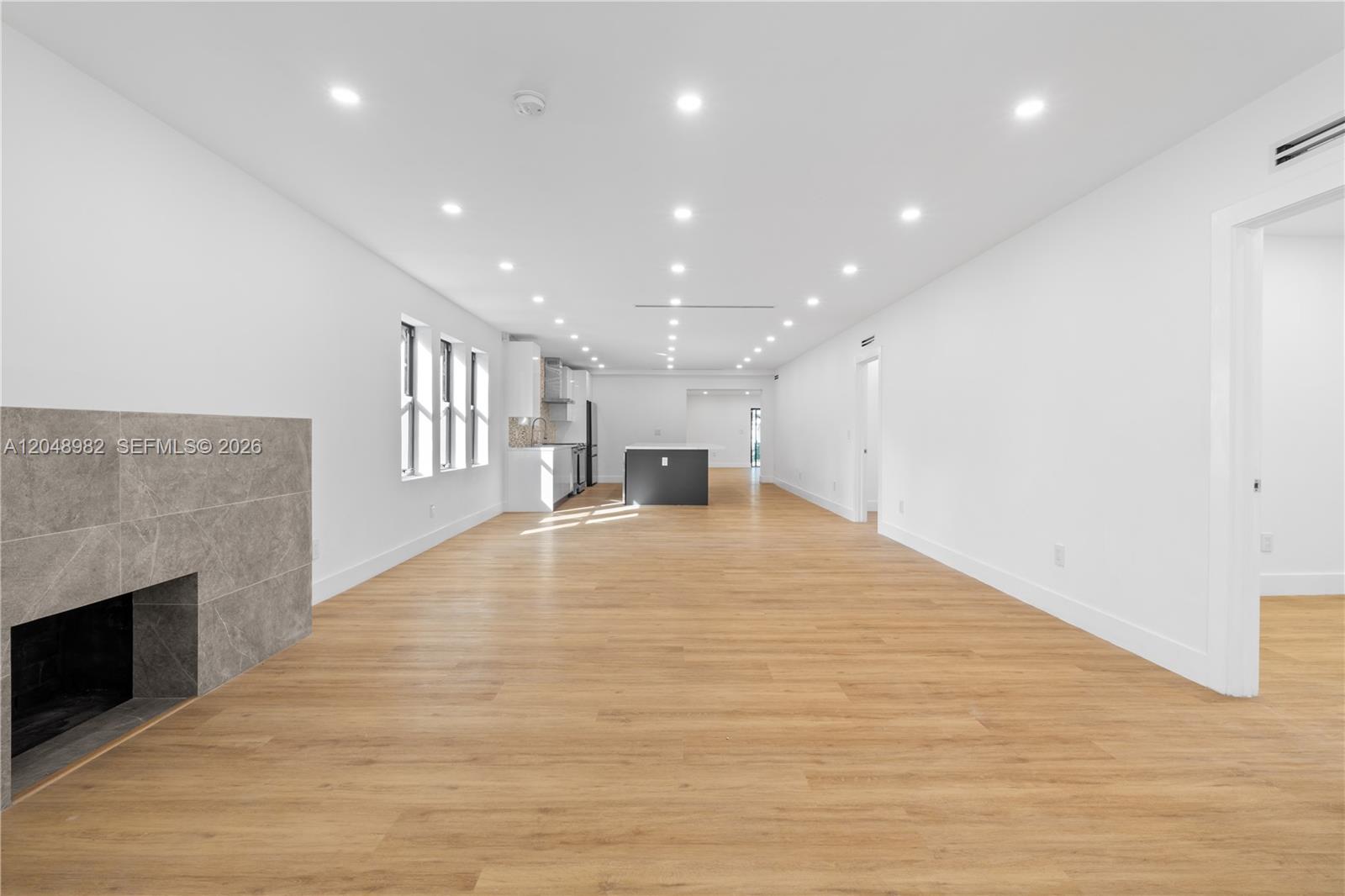 This open-concept living area features light wood flooring, recessed lighting, and a stone fireplace — 665 NE 117th St, Biscayne Park FL 33161, BISCAYNE PARK, FL