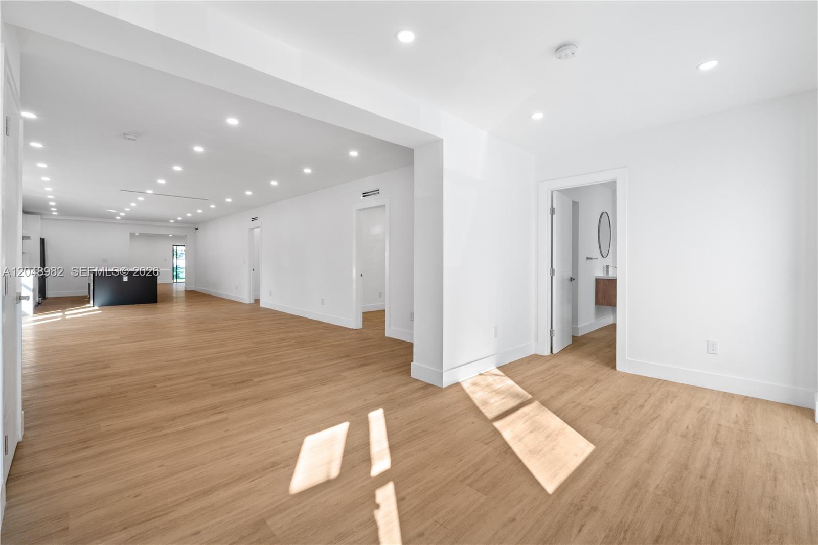An empty, minimalist room features light wood flooring, white walls, and recessed ceiling lighting — 665 NE 117th St, Biscayne Park FL 33161, BISCAYNE PARK, FL