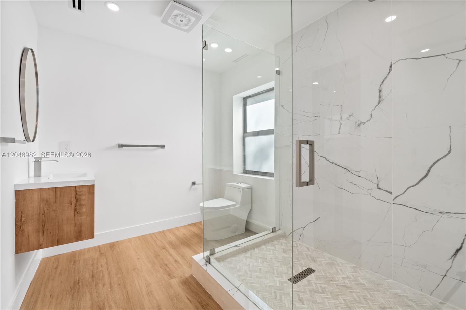 A modern bathroom features a floating wood vanity, a glass-enclosed shower, and marble-patterned wall tiles — 665 NE 117th St, Biscayne Park FL 33161, BISCAYNE PARK, FL