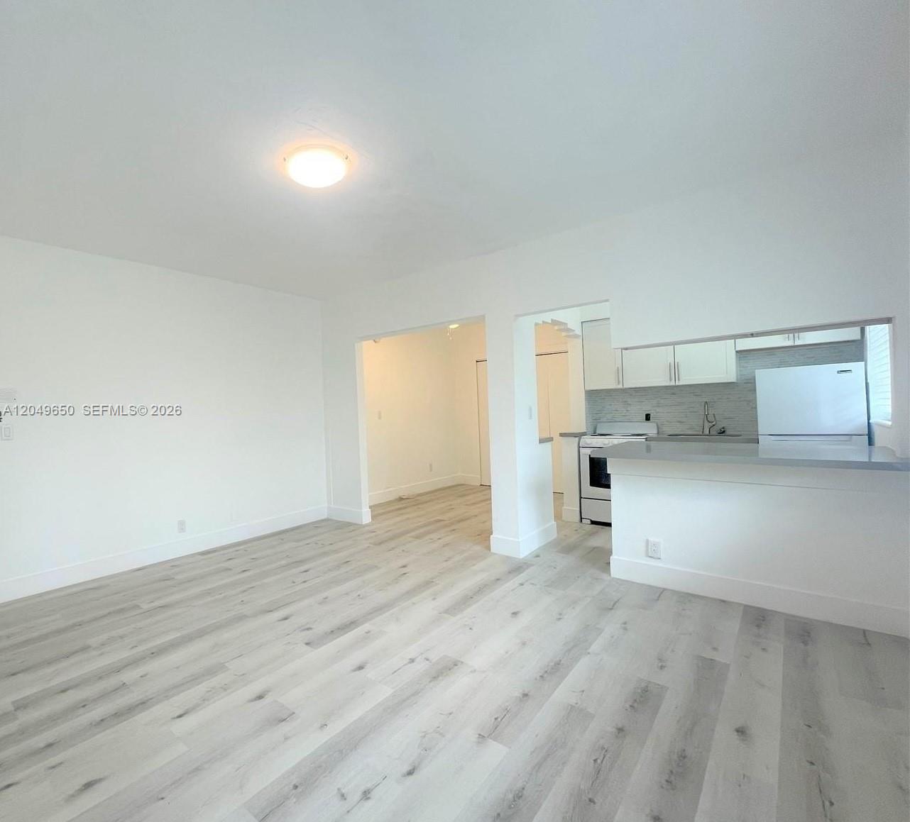 A living room with light wood-look flooring opens into a kitchen with white cabinets — 1021 Euclid Ave # 9, Miami Beach FL 33139, MIAMI BEACH, FL