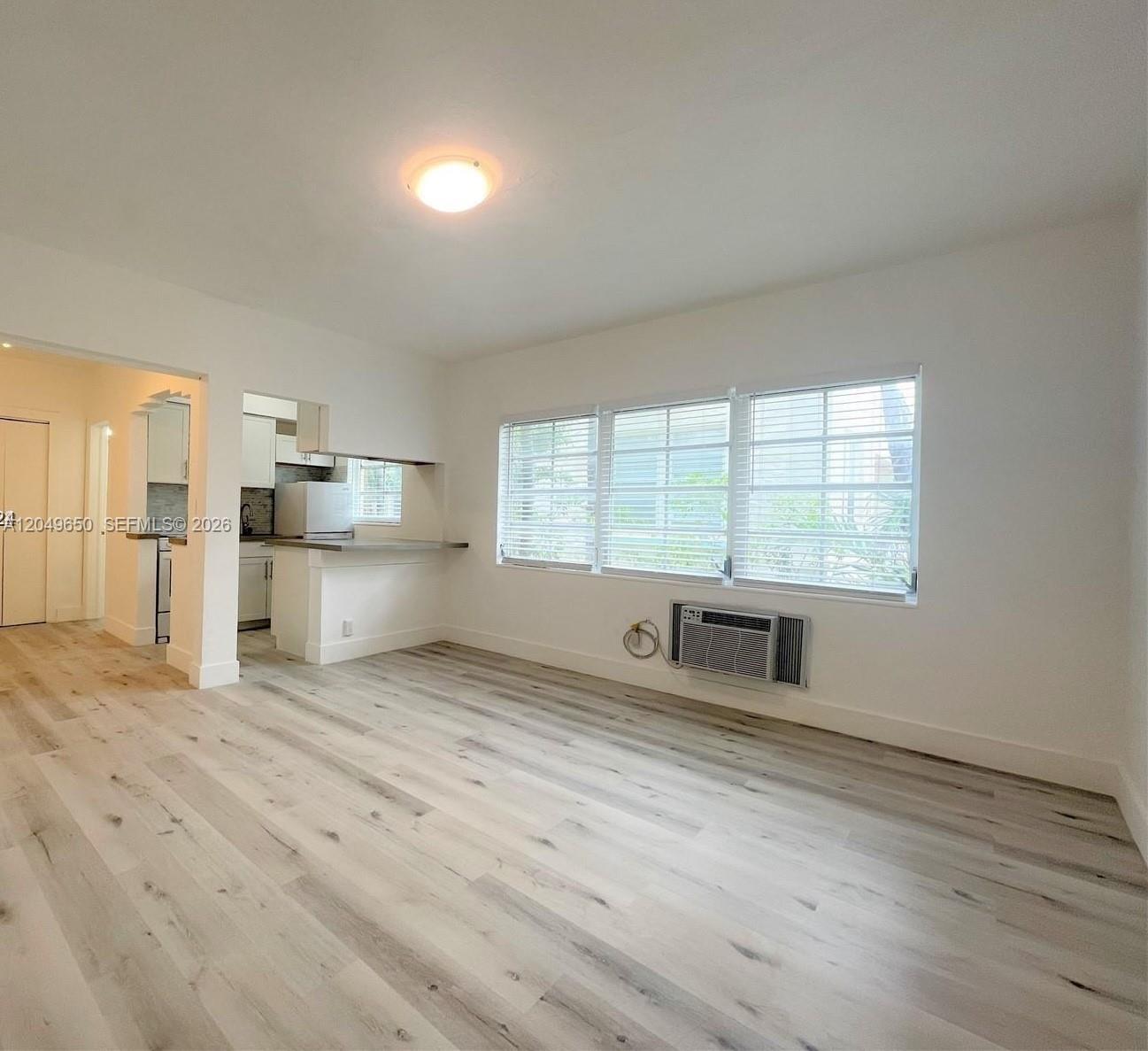 An empty living room features light wood-look flooring, white walls, and a window air conditioner — 1021 Euclid Ave # 9, Miami Beach FL 33139, MIAMI BEACH, FL