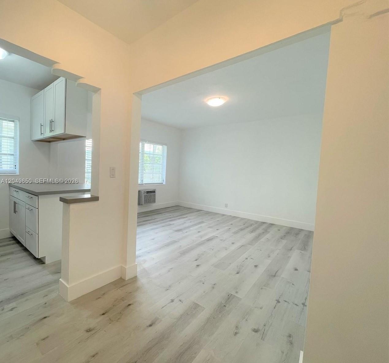 A kitchen with white cabinets opens into a living area with light wood-look flooring — 1021 Euclid Ave # 9, Miami Beach FL 33139, MIAMI BEACH, FL