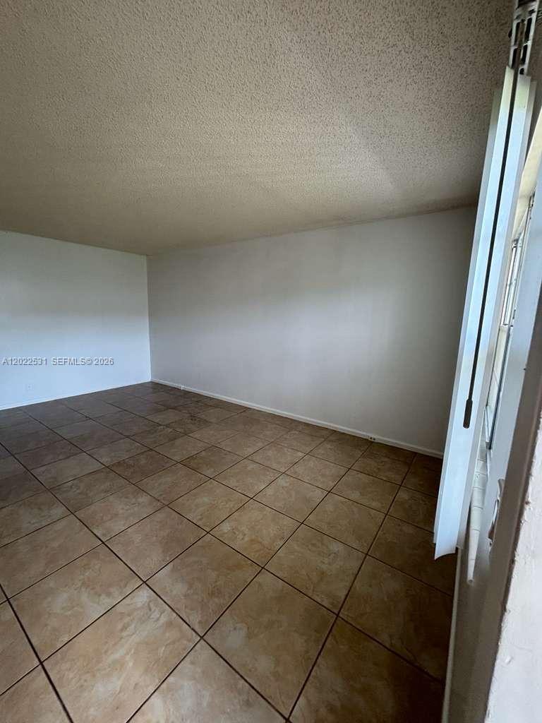 An empty room features beige tile flooring, white walls, and a textured ceiling — 531 Fanshaw M # 531, Boca Raton FL 33434, BOCA RATON, FL