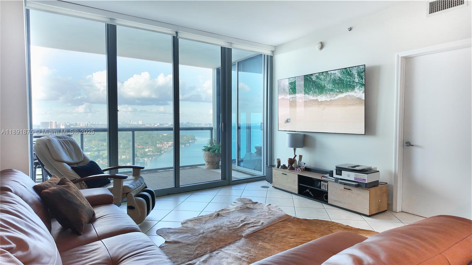 A living room features a leather sofa, a wall-mounted television, and floor-to-ceiling windows overlooking water — 601 NE 36th St # 2206, Miami FL 33137, MIAMI, FL